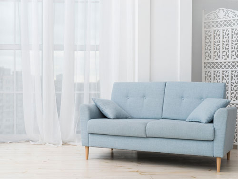 Vista di un salone con divanetto azzurro in primo piano e tende a strascico bianche per dare luminosita all'ambiente
